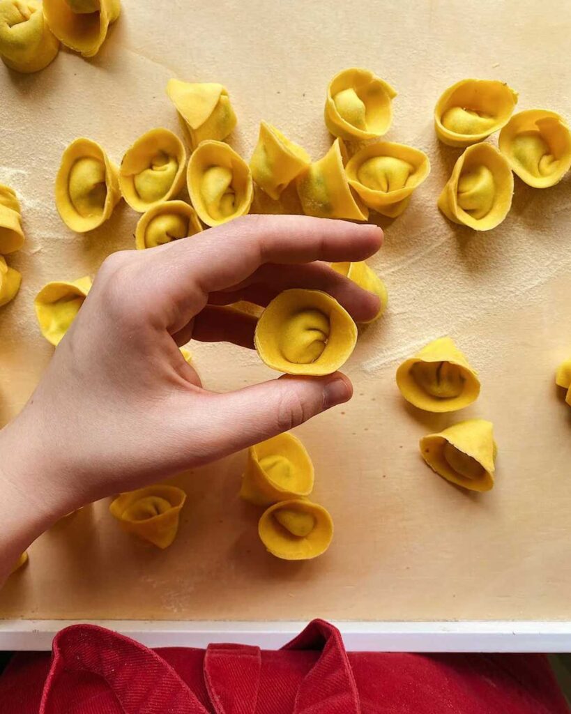 Hand formt frisch zubereitete Tortellini auf einem Holzbrett – traditionelle italienische Pastaherstellung.