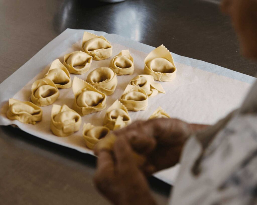 Nahaufnahme einer älteren Person, die selbstgemachte Tortellini auf ein Backblech legt.