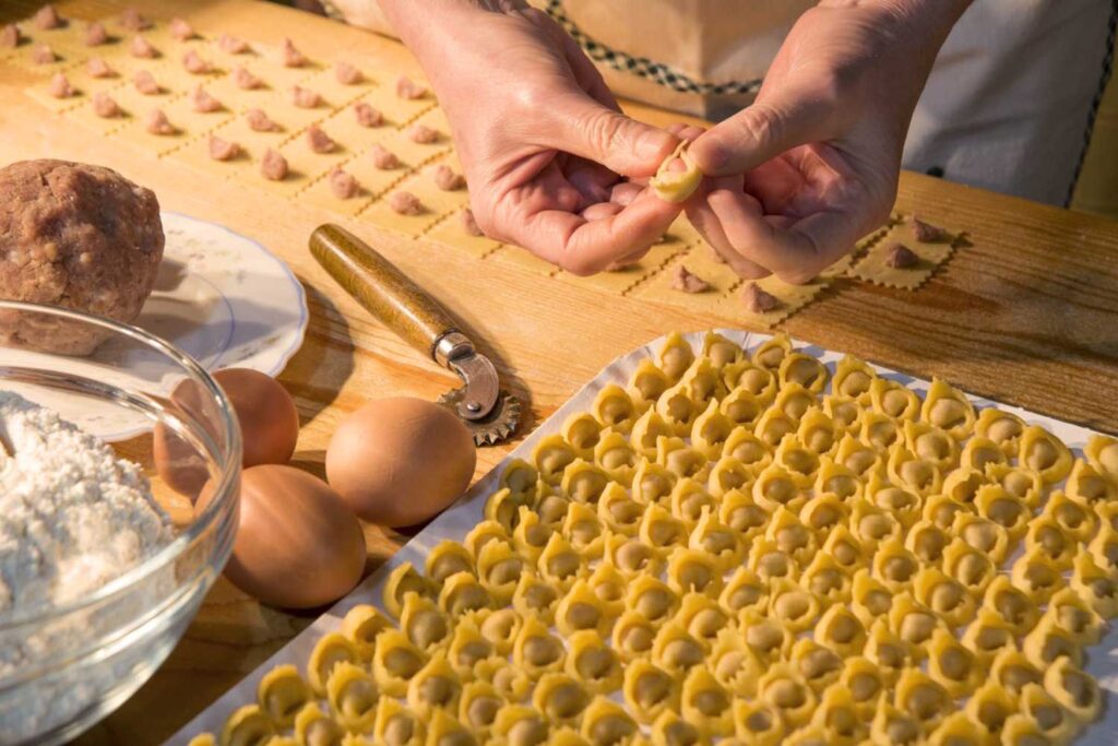 Traditionelle Herstellung von Tortellini mit Fleischfüllung und frischen Eiern auf einem Holztisch.