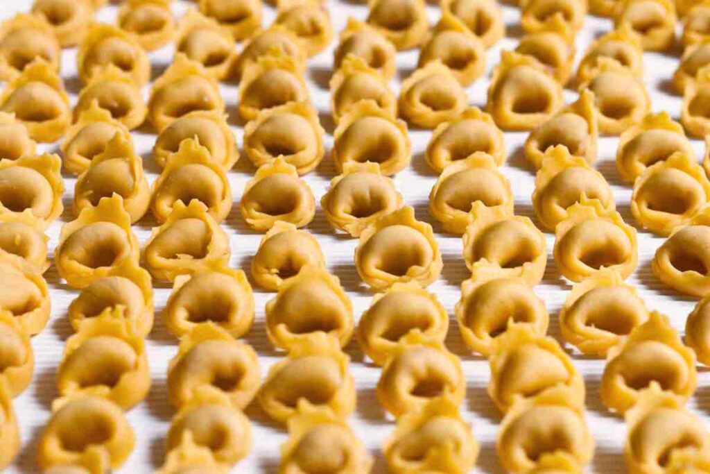 Selbstgemachte Tortellini, aufgereiht und bereit zum Kochen, auf einem hellen Küchentuch.