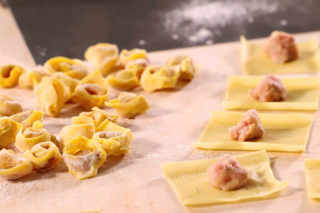 Handgeformte Tortellini auf bemehlter Arbeitsfläche, daneben gefüllte Teigquadrate.