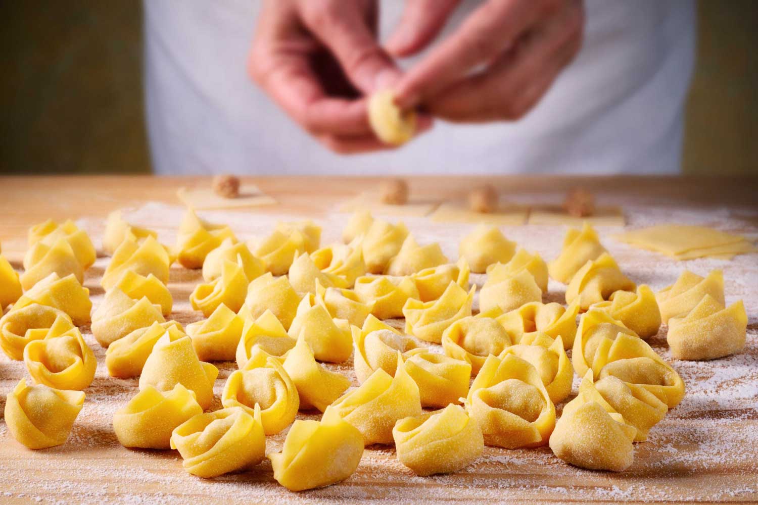 Viele frisch geformte Tortellini liegen auf einer bemehlten Holzfläche, bereit für die Weiterverarbeitung