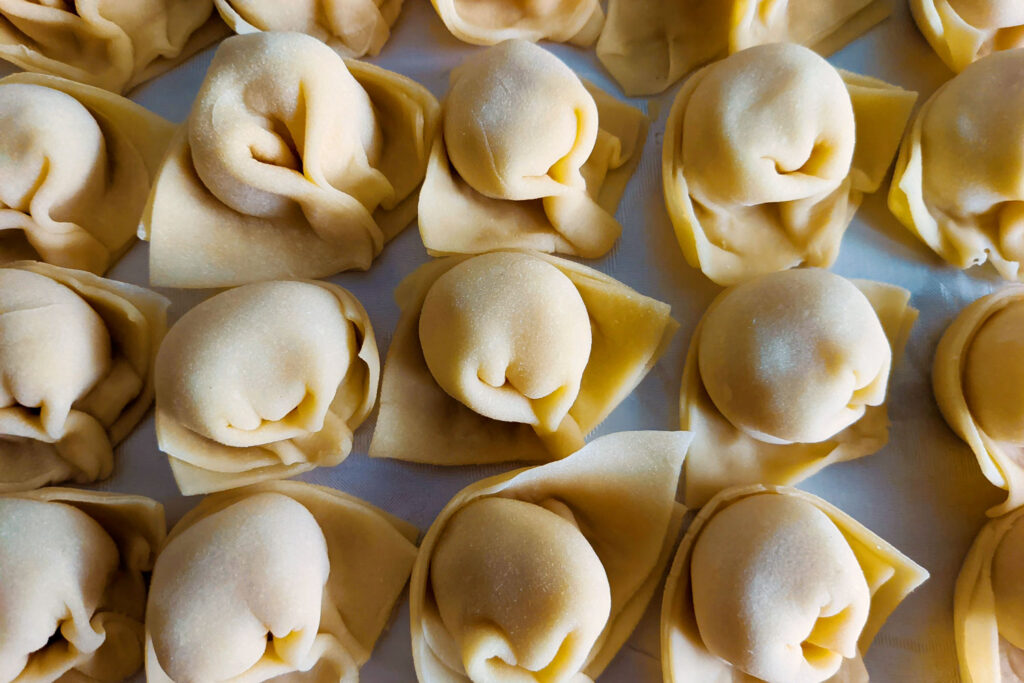 Frisch zubereitete, ungekochte Tortellini auf einem weißen Tuch ausgebreitet.