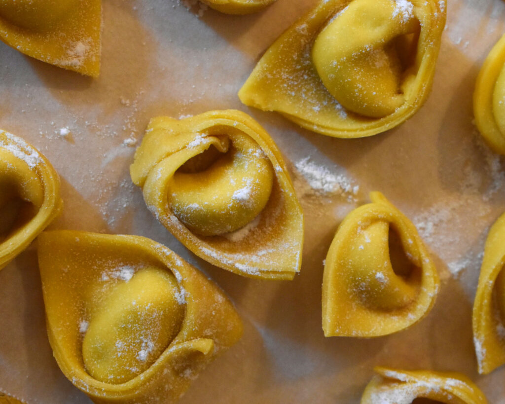 Mit Mehl bestäubte, handgemachte Tortellini auf Backpapier.