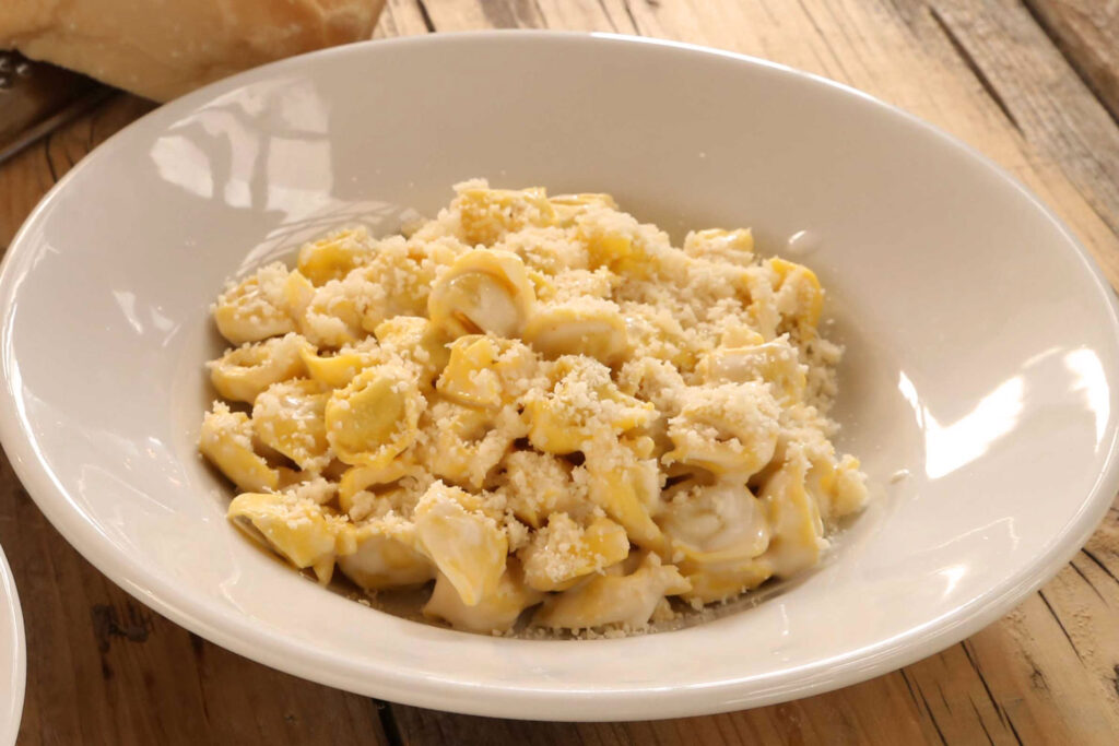 Tortellini mit cremiger Käsesoße und Parmesankäse bestreut, angerichtet in einem weißen Teller.