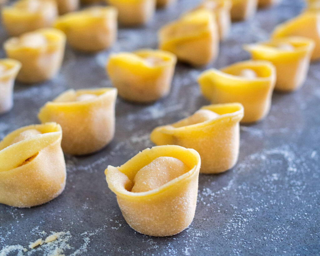 Rohteig-Tortellini auf einem bemehlten Untergrund, bereit zum Kochen.