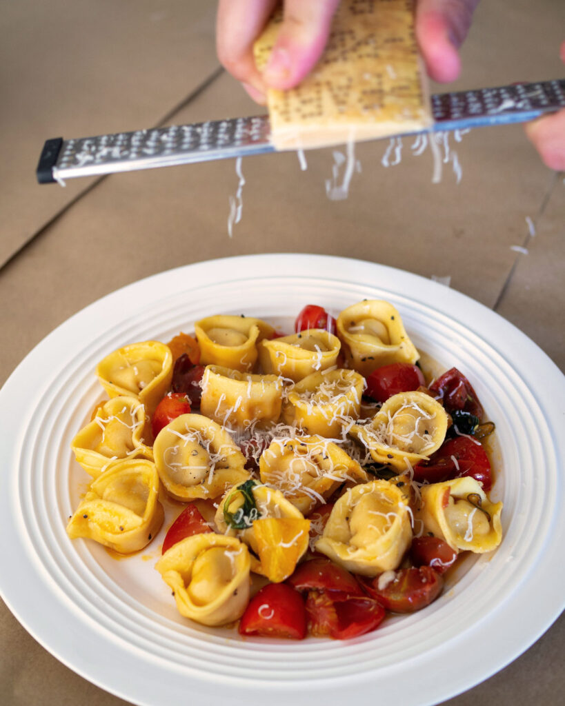 Frische Tortellini mit Tomaten und Kräutern, auf einem Teller angerichtet und mit Parmesan bestreut.