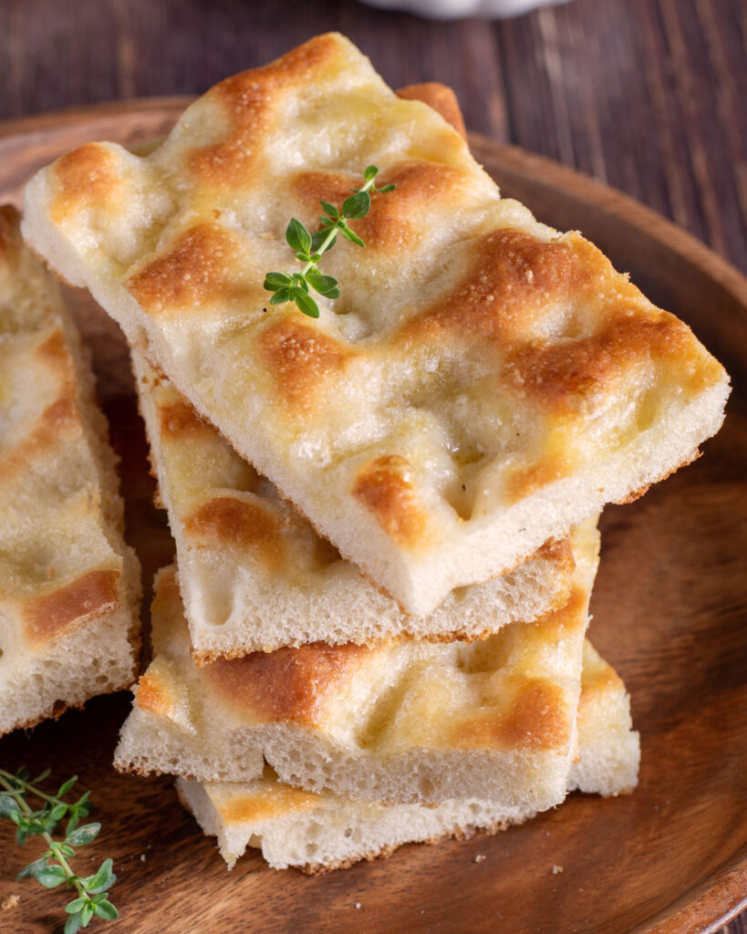 Gestapelte Stücke klassischer Focaccia mit goldener Oberfläche und einem Zweig frischem Thymian.