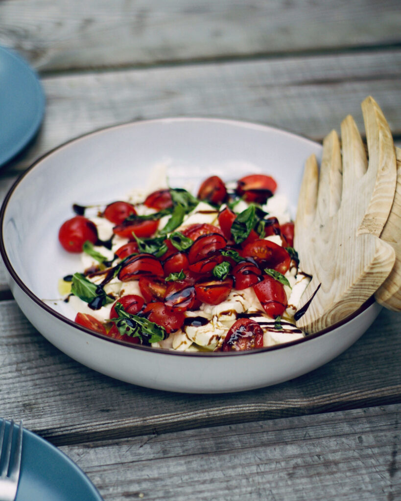 Caprese-Salat mit Cherrytomaten, Mozzarella und Basilikum, angerichtet mit Balsamico auf rustikalem Holztisch.