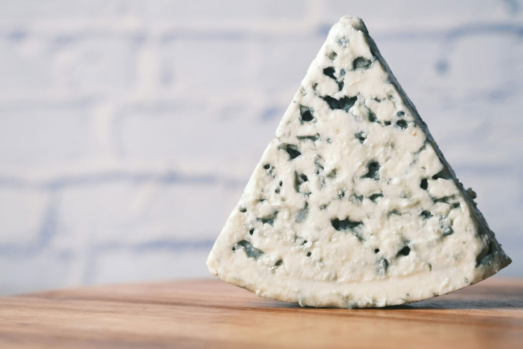 Ein dreieckiges Stück Gorgonzola vor hellem Hintergrund, mit typischer Schimmelstruktur – puristisch in Szene gesetzt.